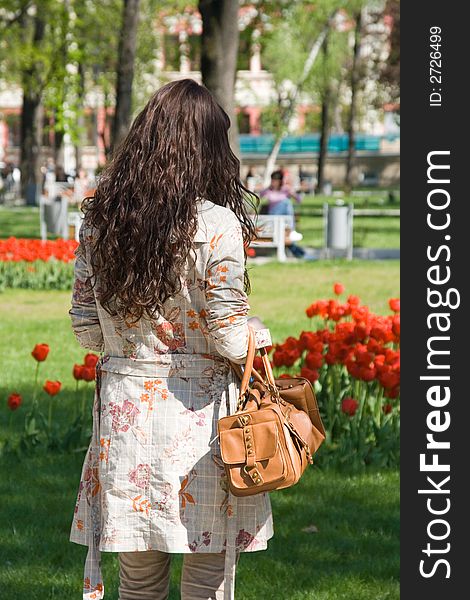 Darkhaired young woman or girl in bright sunshine, standing with her back to us, garden in background. Darkhaired young woman or girl in bright sunshine, standing with her back to us, garden in background