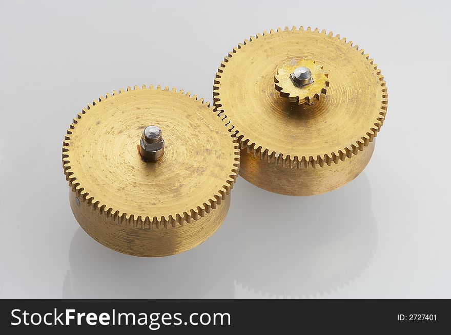 Two old gold-coloured little cogwheels are connected. Two old gold-coloured little cogwheels are connected