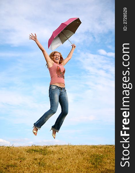 Young woman jumps with the umbrella on to the meadow