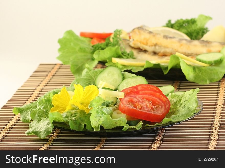 A plate with salad, on a background a dish with fried fish. A plate with salad, on a background a dish with fried fish.
