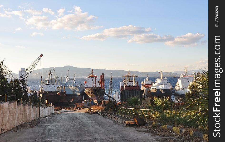 Scrapyard with cranes where large ships docked at the coast waiting for dismantling under blue sky with clouds. AliaaÄŸa, Turkey. Scrapyard with cranes where large ships docked at the coast waiting for dismantling under blue sky with clouds. AliaaÄŸa, Turkey.