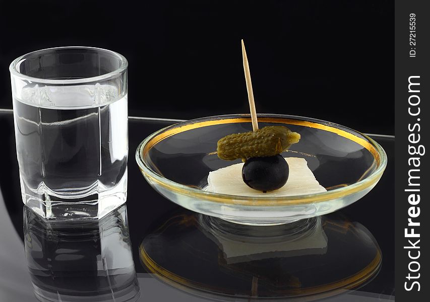 Glass of vodka and dish with snack on black reflective background. Glass of vodka and dish with snack on black reflective background