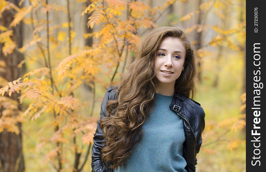 Portrait of smiling girl sitting near the tree in autumn forest