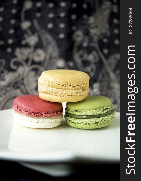 Three color macarons on white plate in black background. Three color macarons on white plate in black background