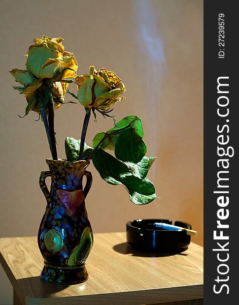 Vase with yellow dried roses and ashtray with cigarette