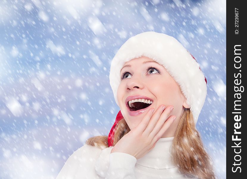 Happy surprised funny girl in a Christmas hat on winter background with snow. Happy surprised funny girl in a Christmas hat on winter background with snow