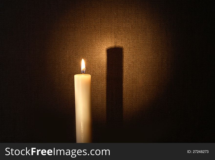 Lighting candle with long shadow against canvas background. Lighting candle with long shadow against canvas background