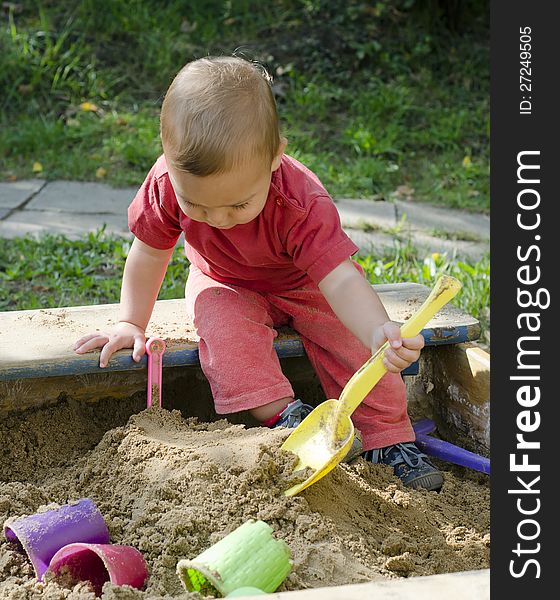 A small child, boy or girl, playing in a sand box with yellow plastic shovel . A small child, boy or girl, playing in a sand box with yellow plastic shovel .