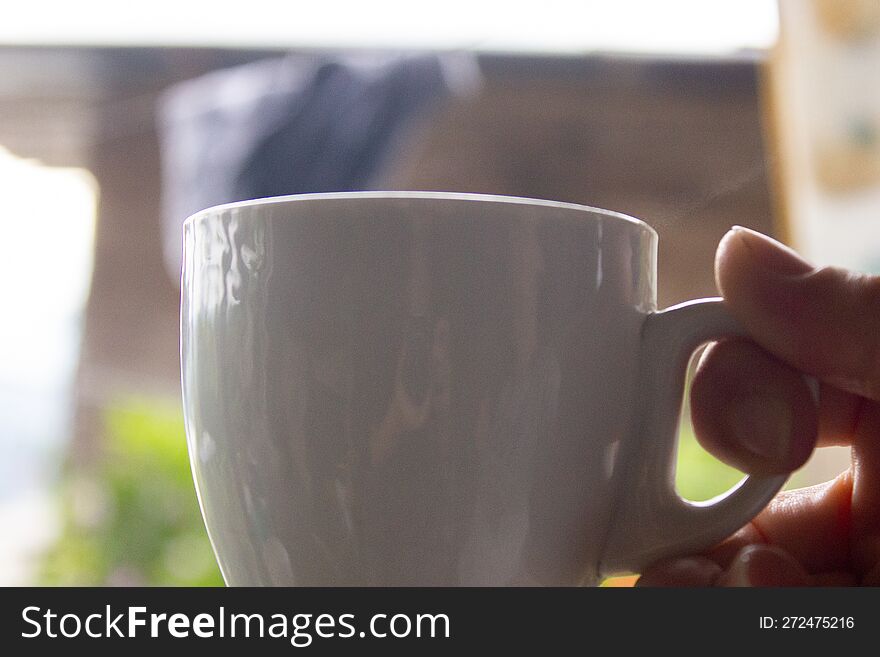 Hand Holding A Cup Of Coffee On The Background Of Green Garden.