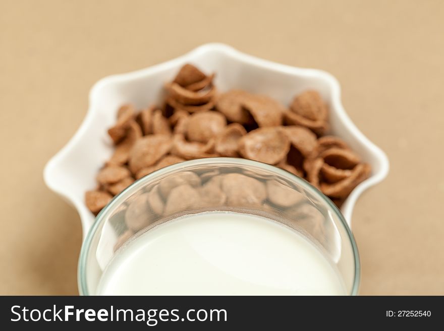 Chocolate cornflakes in white bowl and milk  glass in sepia background. Chocolate cornflakes in white bowl and milk  glass in sepia background