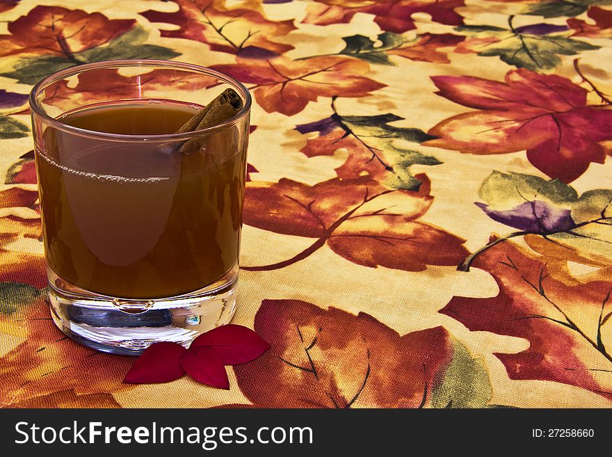 Glass of apple cider with cinnamon stick on autumn table