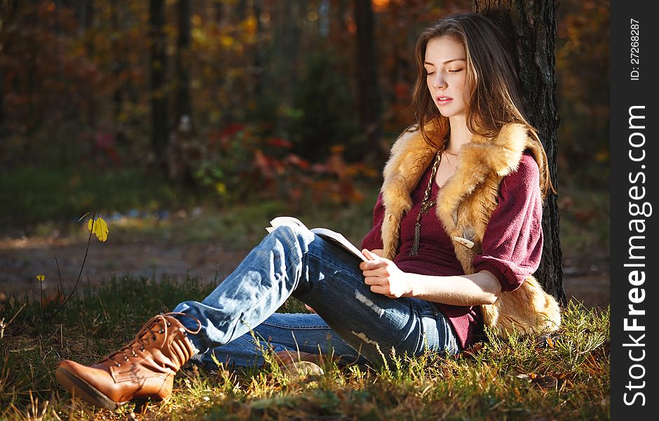 Beautiful autumn girl reading a book in the forest