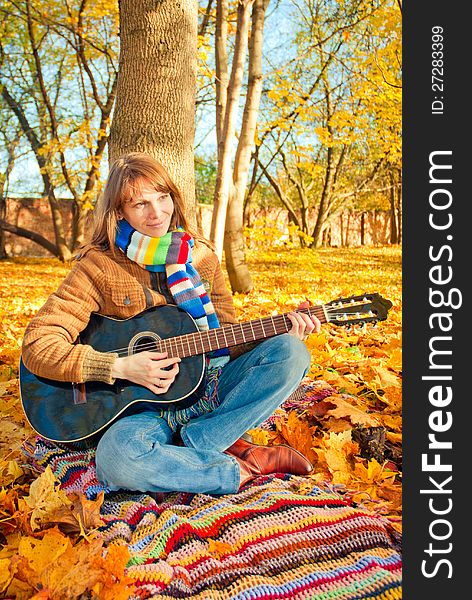 Young romantic girl in autumn park with guitar