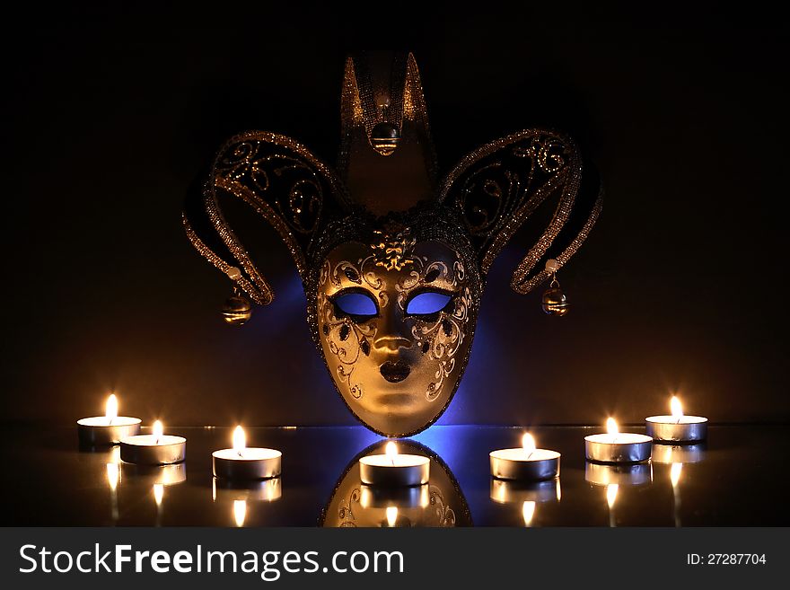 Beautiful classical venetian mask near lighting candles on dark background. Beautiful classical venetian mask near lighting candles on dark background