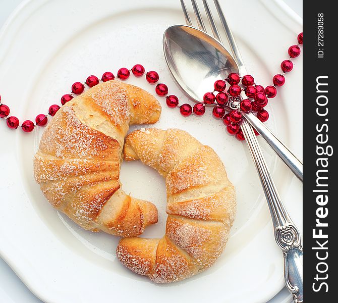 Croissanton on a White Plate with Spoon Fork and Red Beads. Croissanton on a White Plate with Spoon Fork and Red Beads