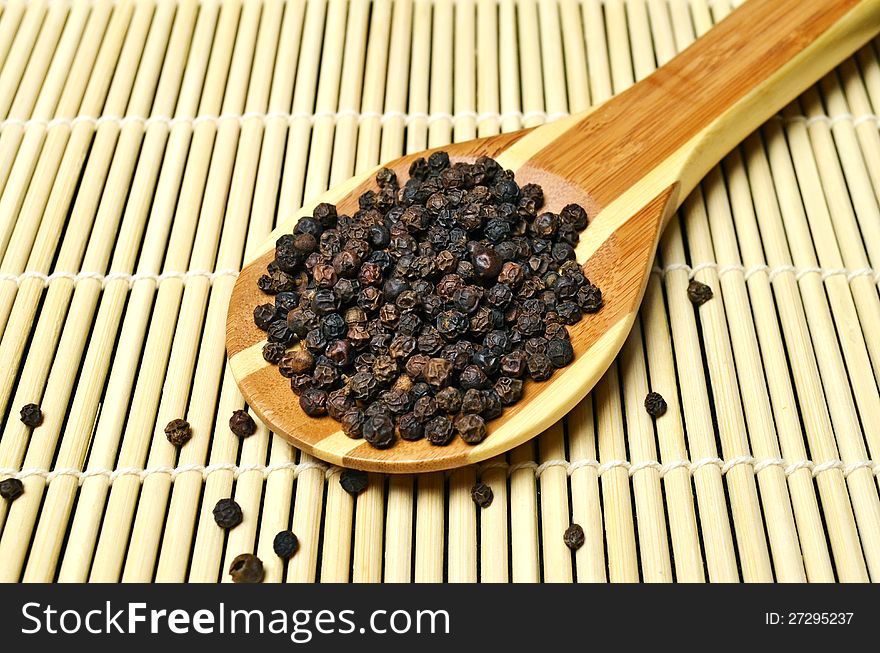 Black peppercorns in wooden spoon on bamboo background