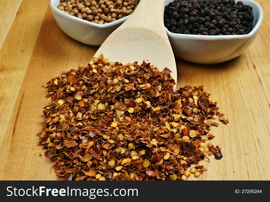 Red chili pepper flakes in spoon on wooden background