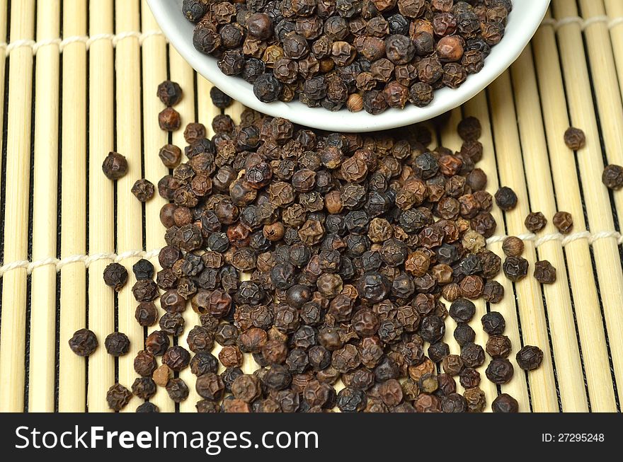 Black peppercorns and seeds falling from a white bowl