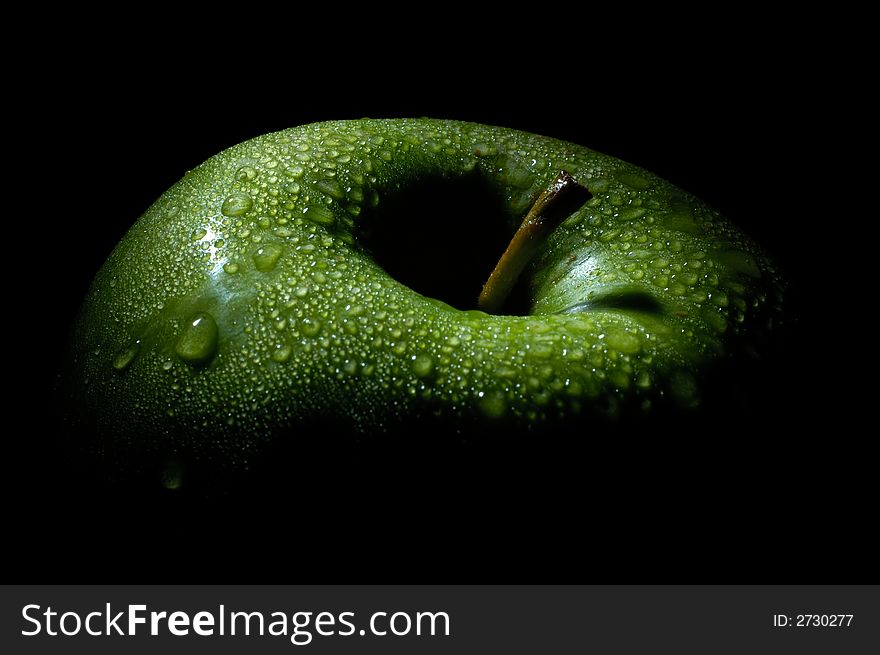 Image shows a green fresh apple in the dark, only lit by one spot light on top. Image shows a green fresh apple in the dark, only lit by one spot light on top.