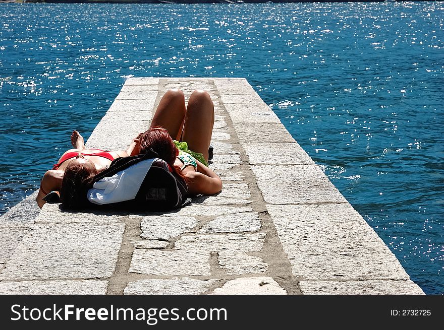 Two girls suntanning on a dock.