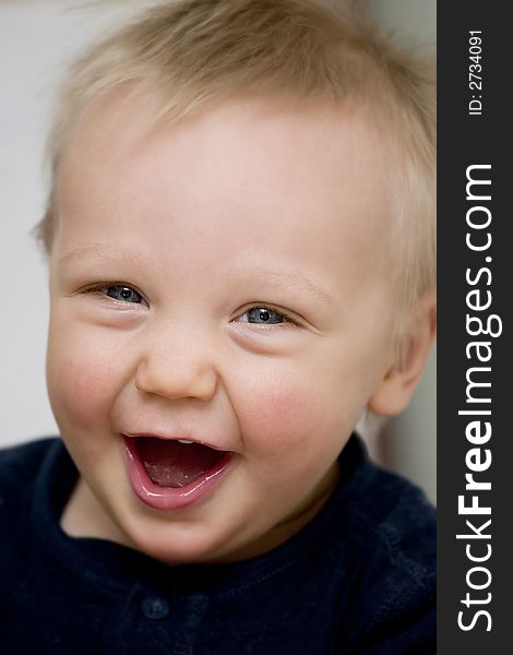 A blue-eyed baby boy in a dark blue shirt is laughing at the camera. A blue-eyed baby boy in a dark blue shirt is laughing at the camera.