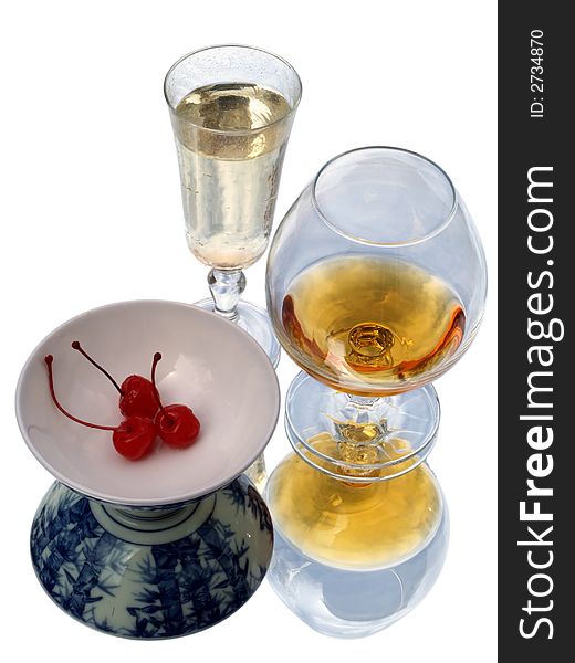 Still life with brandy glass, champagne flute and bowl of cherries. Reflected and isolated.