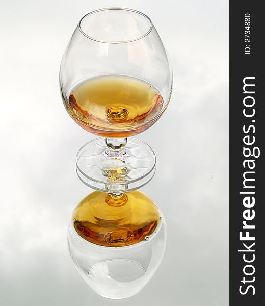 Still life with brandy glass. Reflected with cloud texture background.