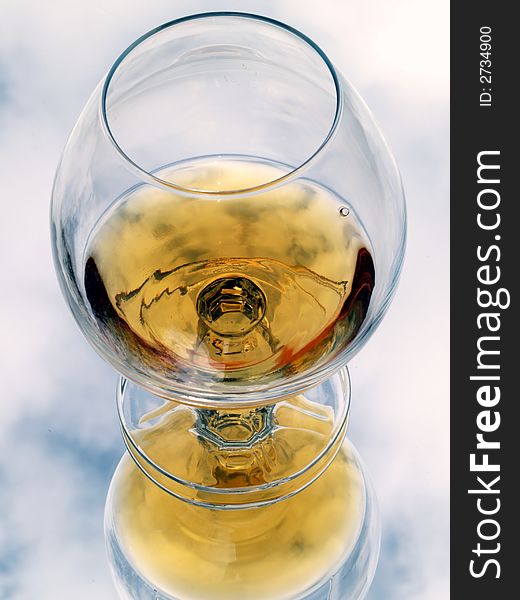 Still life with brandy glass. Reflected with cloud texture background.