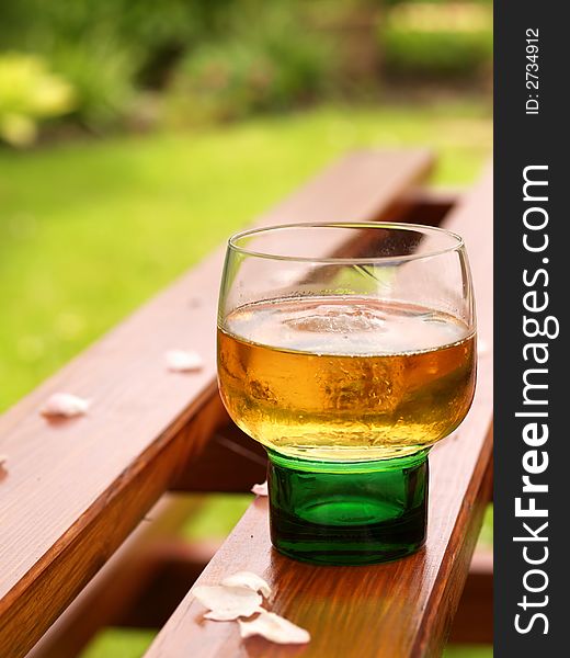 Drink in a green glass on a picnic table with garden as backdrop. Drink in a green glass on a picnic table with garden as backdrop