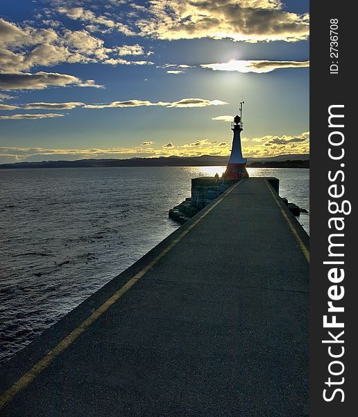 Breakwater with a lighthouse silhouette against sunset. Breakwater with a lighthouse silhouette against sunset