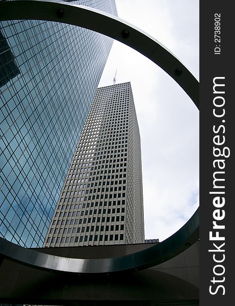 Two large skyscrapers towering above a large decorative ring on a much shorter structure. Two large skyscrapers towering above a large decorative ring on a much shorter structure.