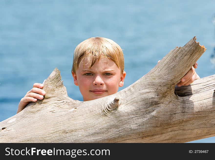 Young boy looking over driftwood with OOF water and sky background