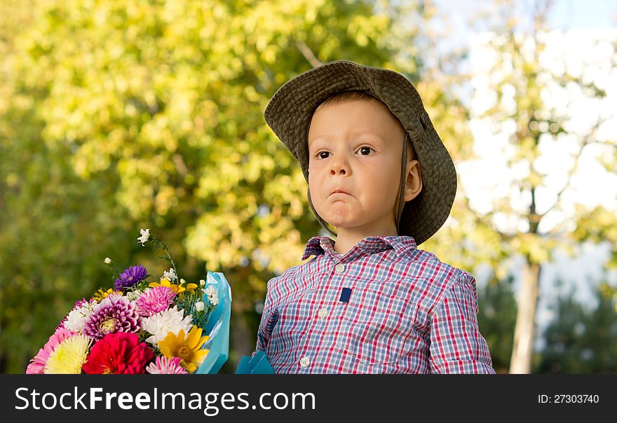 Bemused little boy pulling a funny expression holding a bunch of flowers for his mother on Mothers Day or Valentines with copyspace. Bemused little boy pulling a funny expression holding a bunch of flowers for his mother on Mothers Day or Valentines with copyspace