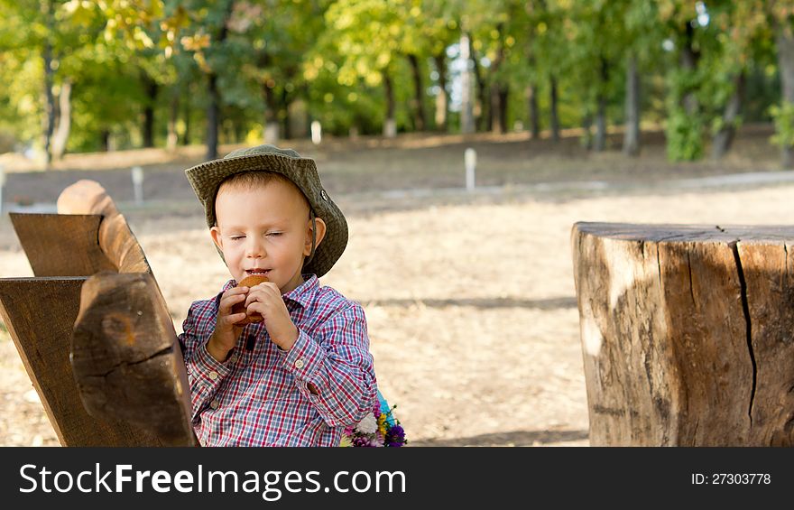 Little boy in a cowboy style hat enjoying a snack outdoors in a park with woodland. Little boy in a cowboy style hat enjoying a snack outdoors in a park with woodland