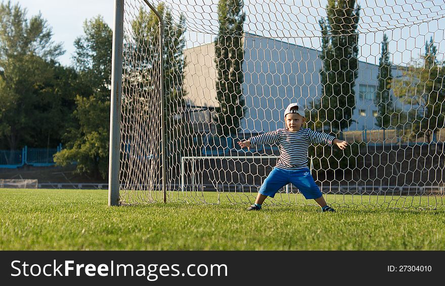 Young little goalie wearing a backwards cap standing in the goals with his legs and arms spread wide protecting the goal line
