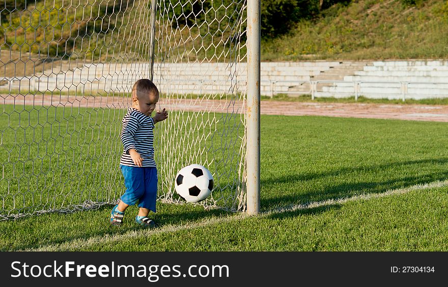 Little boy playing at being a goalkeeper kicking a soccer ball away from the goal line on a green playing field. Little boy playing at being a goalkeeper kicking a soccer ball away from the goal line on a green playing field