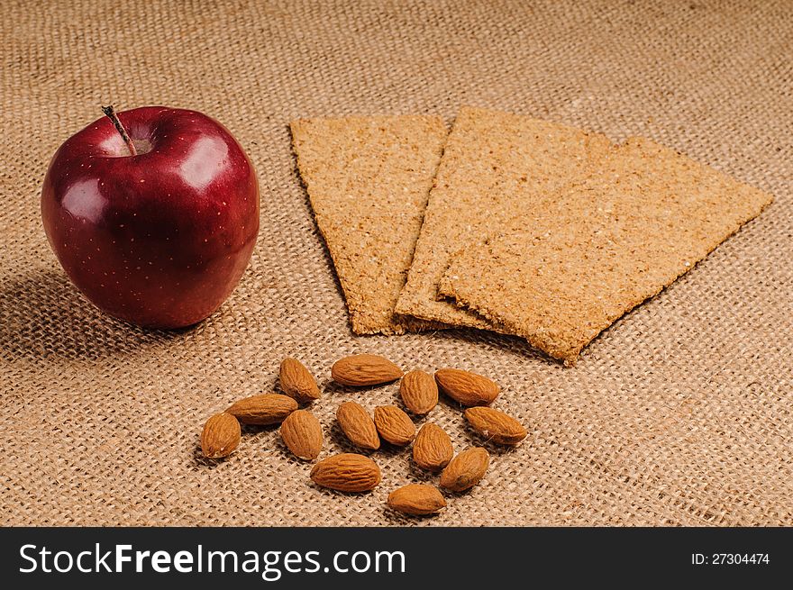 Red apple with crispbread and almonds on sacking background