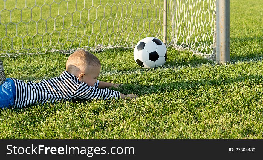 Small boy lies stretched out on the green grass in the goals as he misses the ball while playing goalkeeper,. Small boy lies stretched out on the green grass in the goals as he misses the ball while playing goalkeeper,