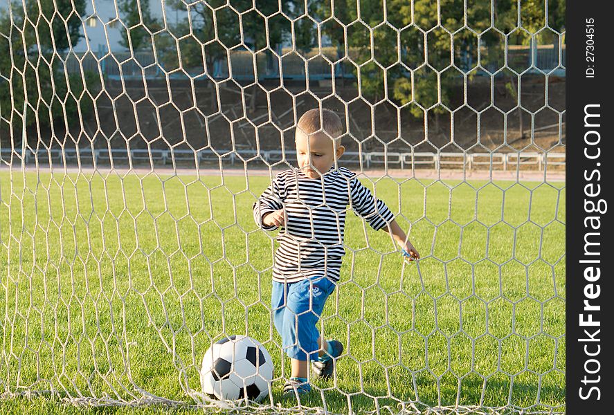 View through the net of a little boy running up to the goalposts and kicking a goal. View through the net of a little boy running up to the goalposts and kicking a goal