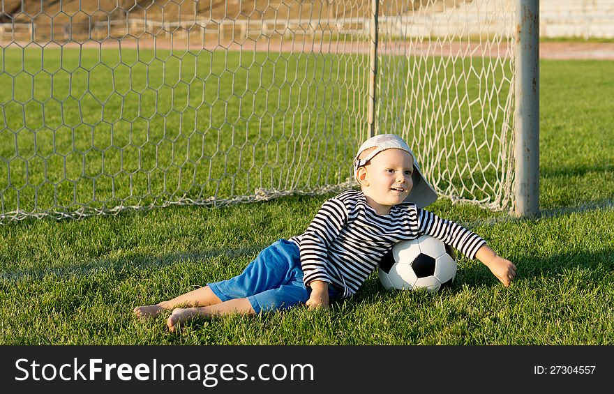Barefoot youngster with soccer ball lying on green grass in front og goalposts on a green grassy sportsfield