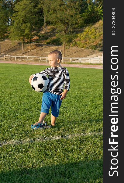 Small boy standing waiting with his soccer ball on a gren grass sportsfield in evening light. Small boy standing waiting with his soccer ball on a gren grass sportsfield in evening light