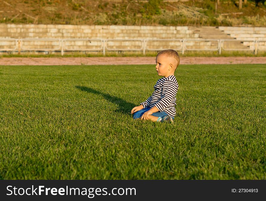 Small boy kneeling in green grass in evening sunlight