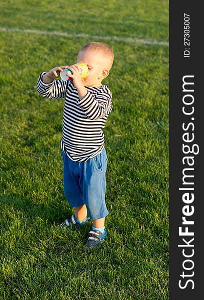 Little boy standing on green grass holding a cup in both hands enjoying a refreshing drink. Little boy standing on green grass holding a cup in both hands enjoying a refreshing drink