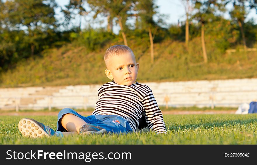 Low angle view of a cute little boy lying on his back on green grass in evening sunlight. Low angle view of a cute little boy lying on his back on green grass in evening sunlight