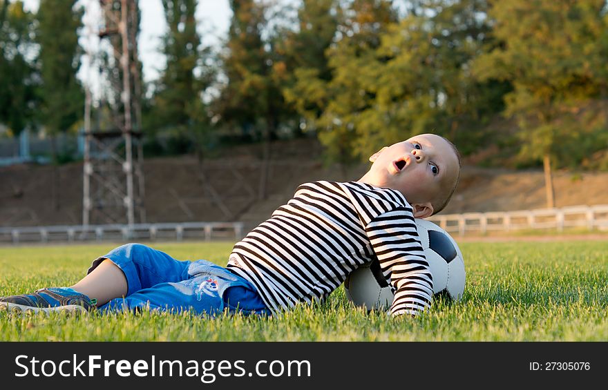 Small boy lying on his back on green grass with his head resting on a soccer ball playing around. Small boy lying on his back on green grass with his head resting on a soccer ball playing around