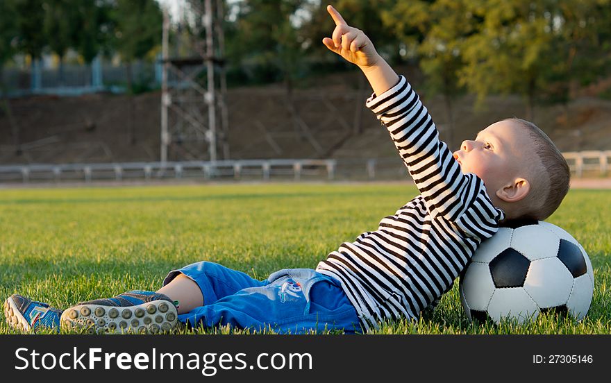 Little boy lying on his back in green grass with his head resting on a soccer ball pointing at the sky. Little boy lying on his back in green grass with his head resting on a soccer ball pointing at the sky