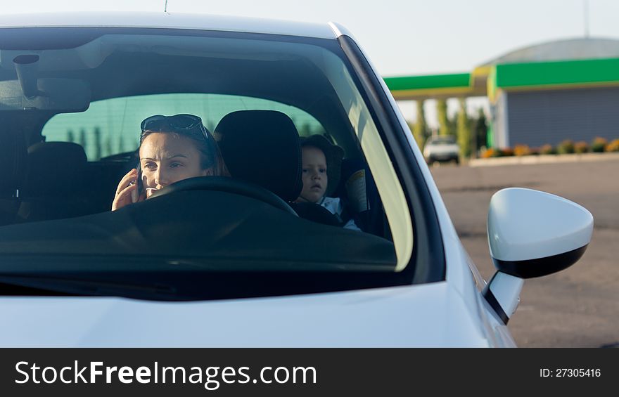 View through the windscreen of a woman using mobile phone in a car with her young son sitting in the back as a passenger. View through the windscreen of a woman using mobile phone in a car with her young son sitting in the back as a passenger