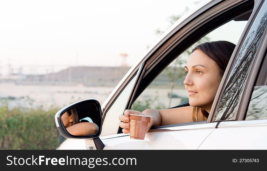 Woman sitting in car with her arm through the open window and a plastic cup with a drink in her hand. Woman sitting in car with her arm through the open window and a plastic cup with a drink in her hand