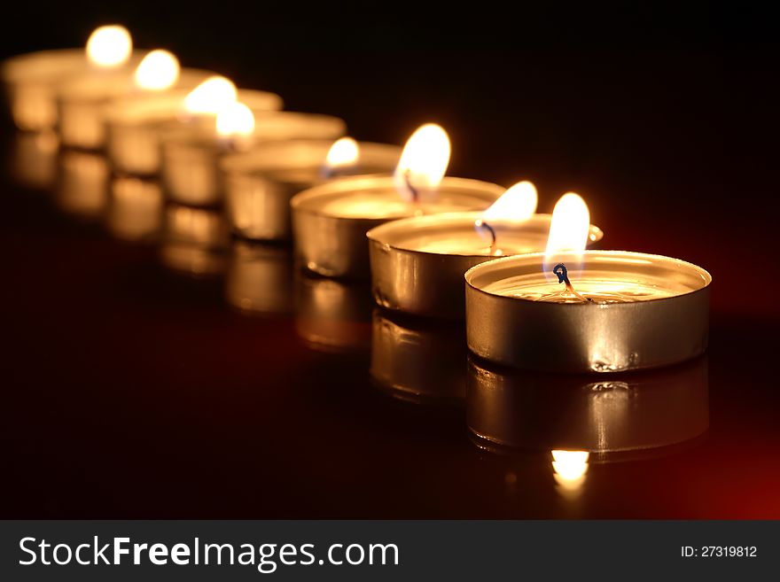 Set of lighting candles in a row on dark background with reflection. Set of lighting candles in a row on dark background with reflection