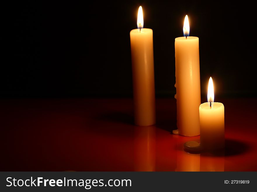 Three lighting candles on dark background with reflection